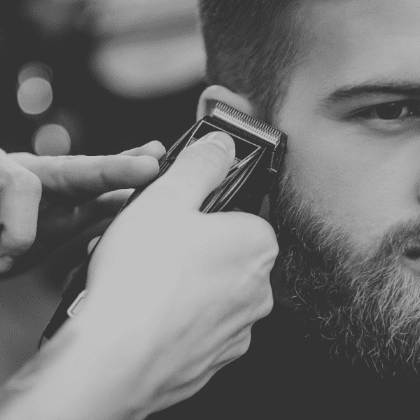 Barber using clippers to trim a man's beard in a close-up shot.