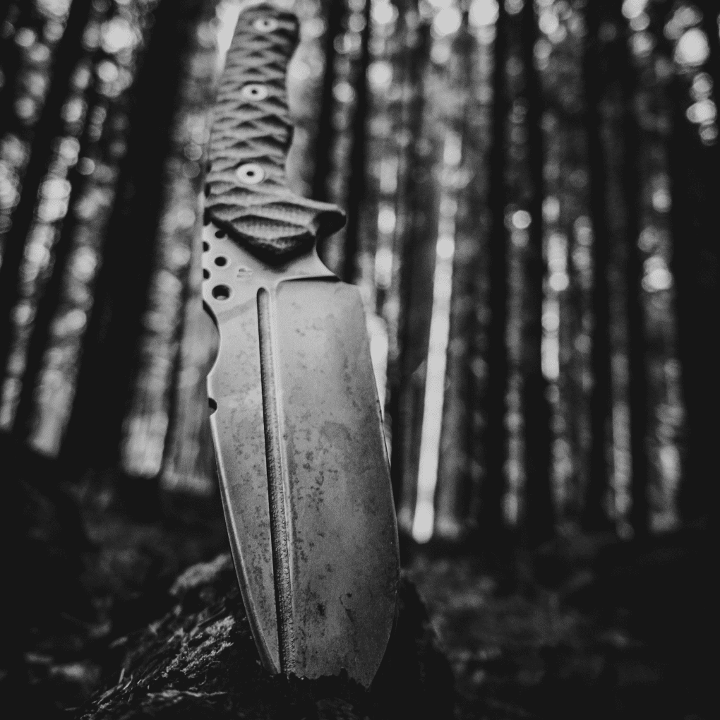 Knife with textured handle in a forest, black and white image.