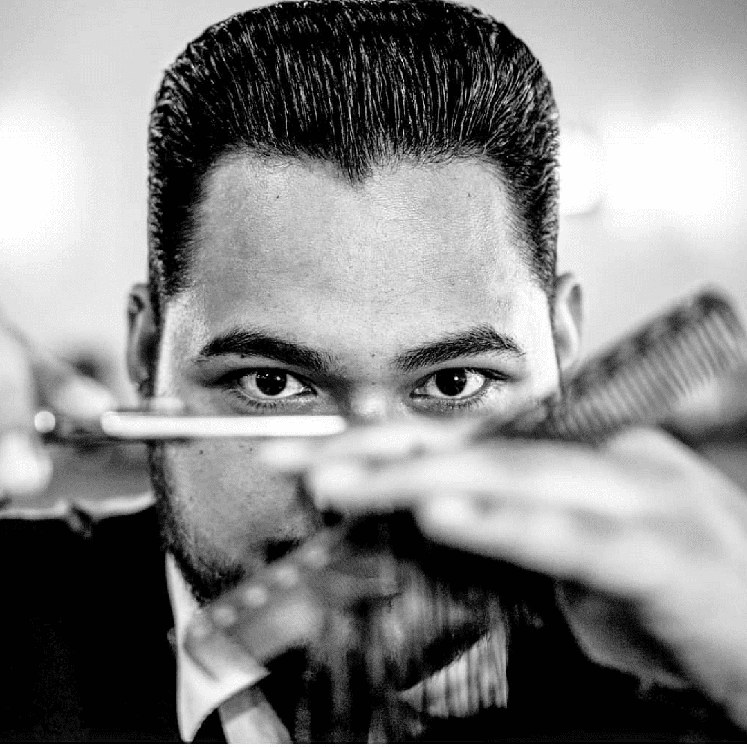 Barber concentrating while cutting hair with scissors and a comb, black and white photo.