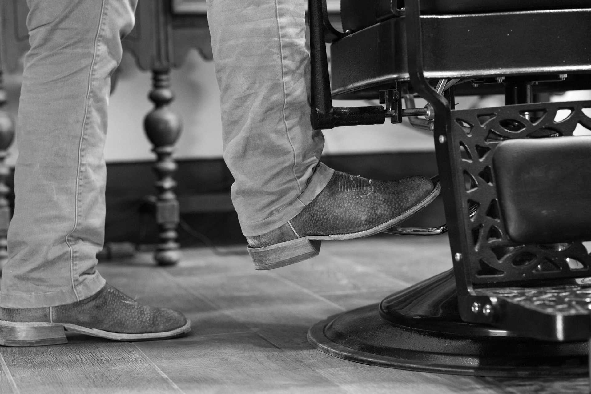 Barber chair footrest with man's foot pressing down, wooden floor visible.