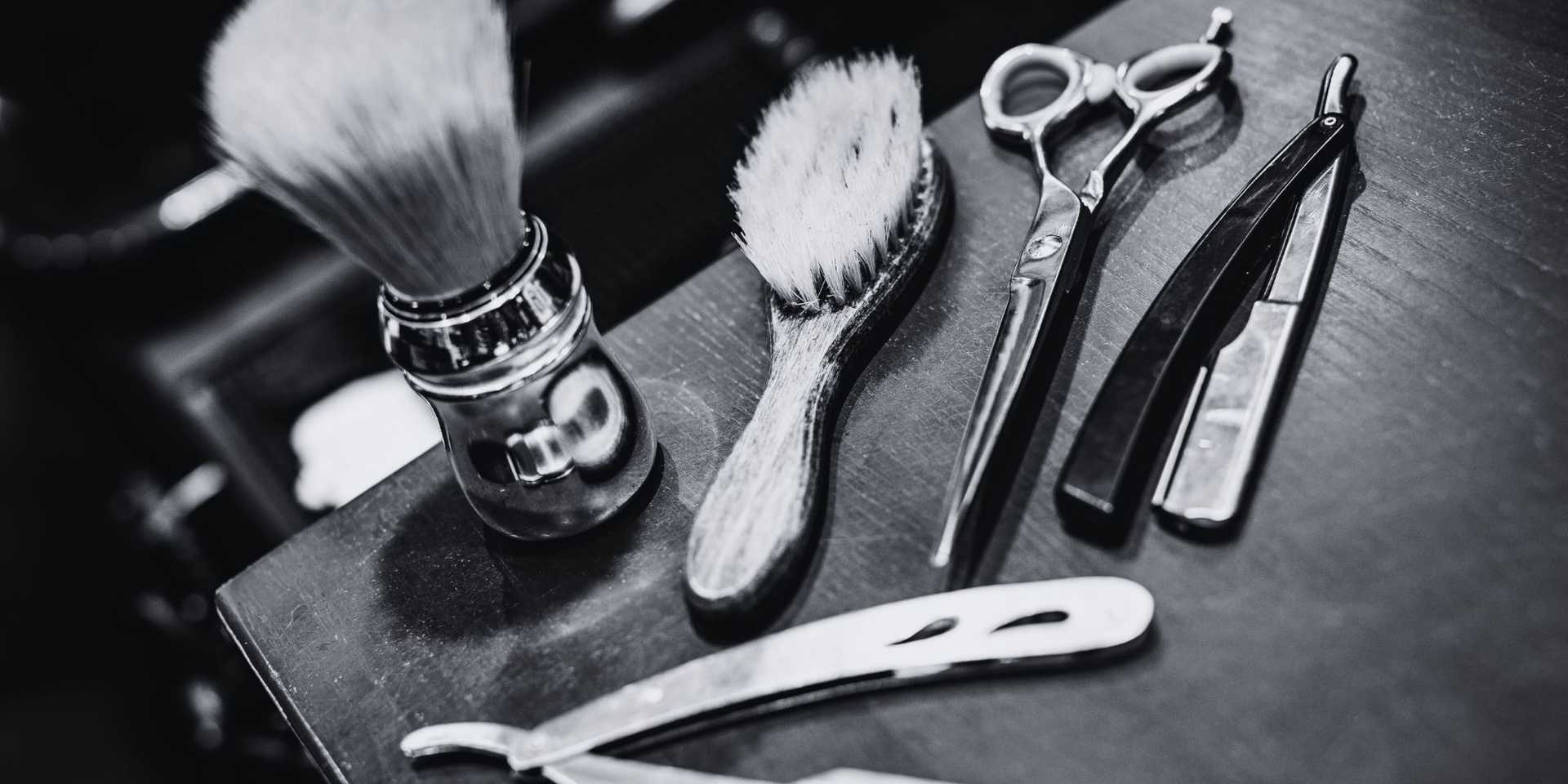 Vintage barber tools, including razors, scissors, brushes, and a shaving brush on a wooden surface.